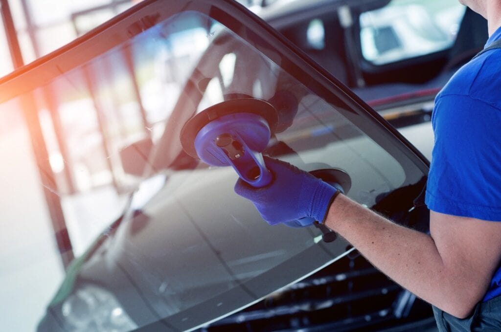 Automobile special workers replacing windscreen or windshield of a car in auto service station garage.