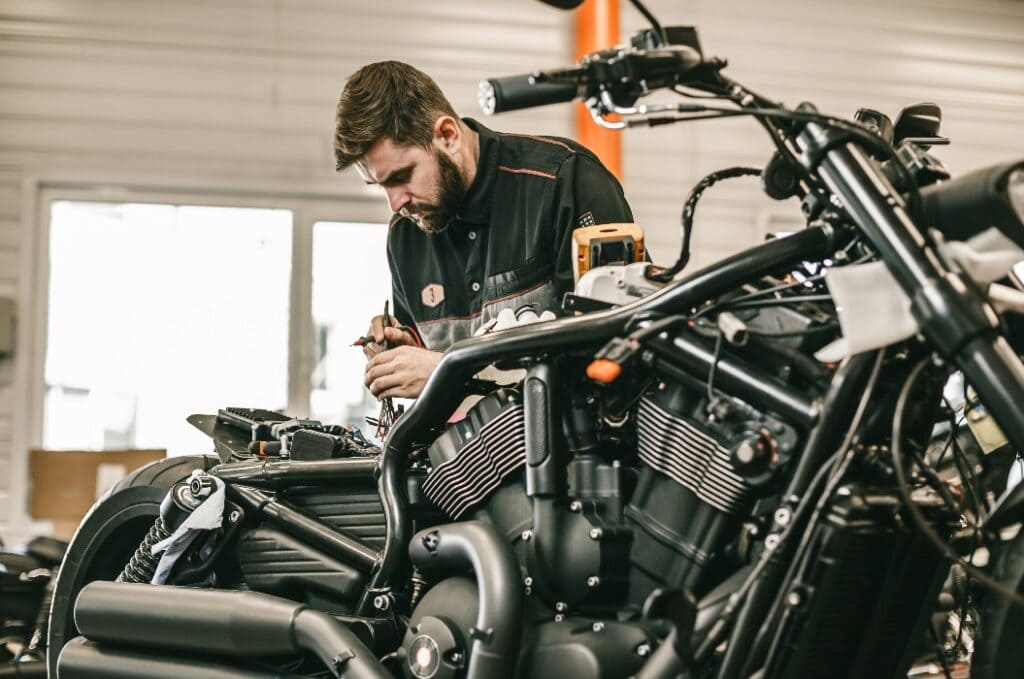 Motorcycle mechanic repairing electronics sports black bike. Handsome mechanic working in auto repair shop.